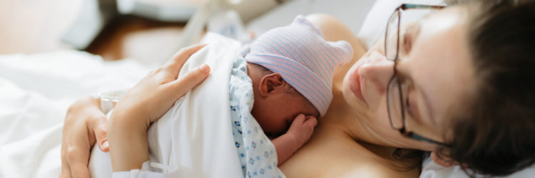 newborn baby in hospital after just being born, mother holding him and breastfeeding in hospital bed