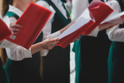 Church choir concert in cathedral, choral artists singing, group of European boys and girls singing in a chorus, students and choristers in white and green uniform performing on stage with conductor